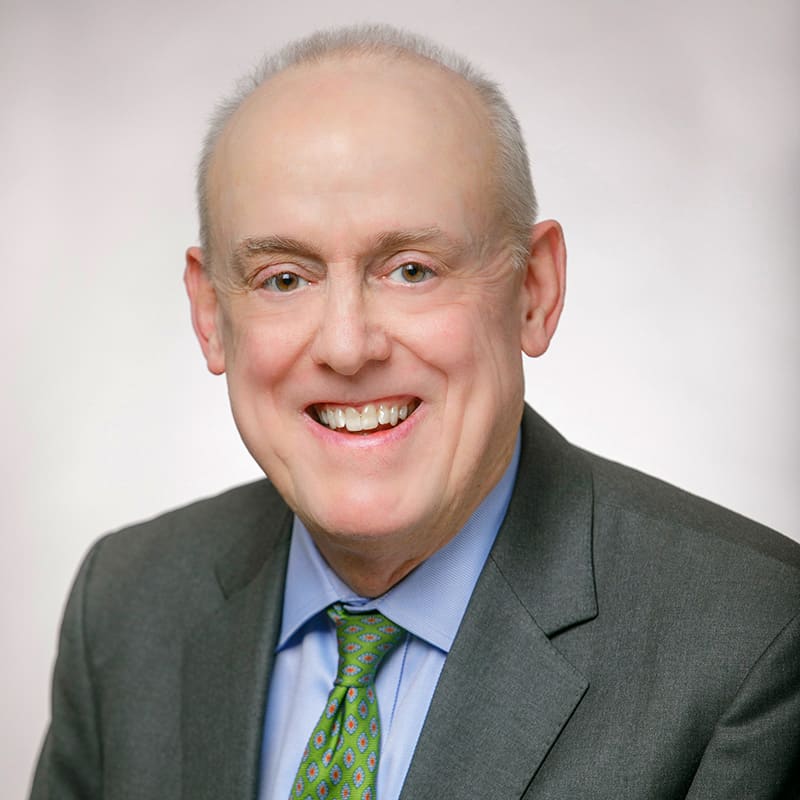 Portrait of Richard Patterson wearing a charcoal suit and a holly-green tie.